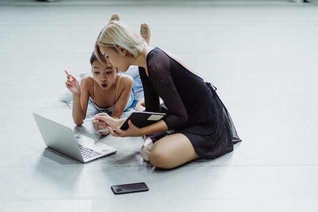 Impressed Asian little ballerina with instructor using laptop