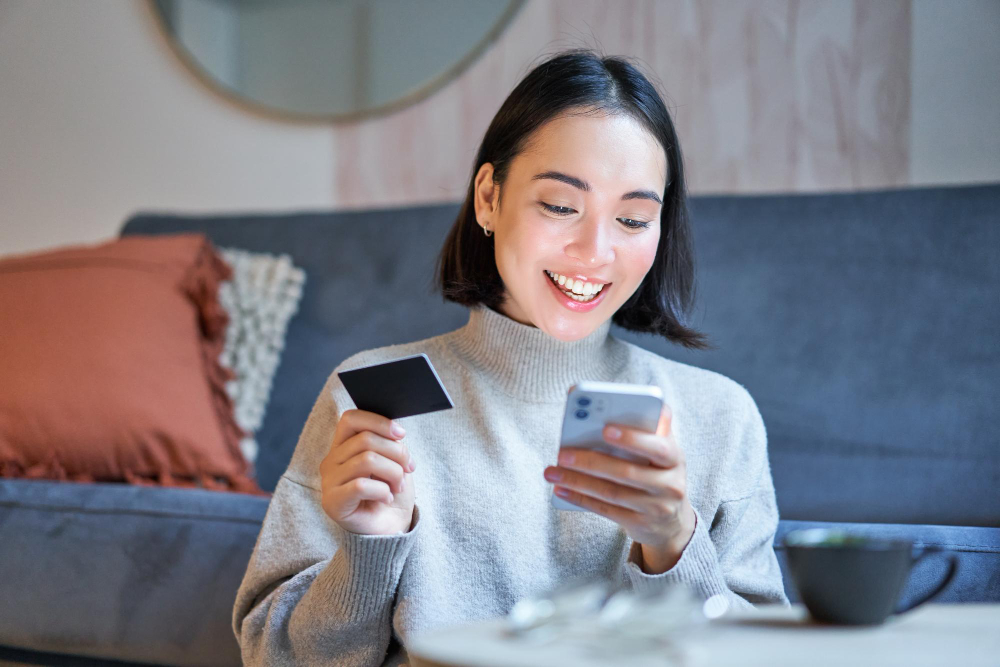 kode bank dana: potret wanita korea yang tersenyum menggunakan aplikasi ponsel pintar kartu kredit membayar pesanan pembelian secara online
