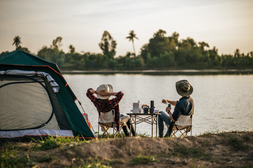 Tahun baru anti mainstream: rear view young backpacker couple sitting relax front tent near lake with coffee set making fresh coffee grinder while camping trip summer vacation